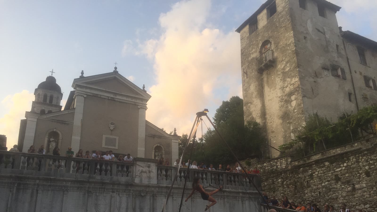 Spettacolo di strada nel centro storico di Feltre, il pubblico affacciato alla balaustra sotto la torre