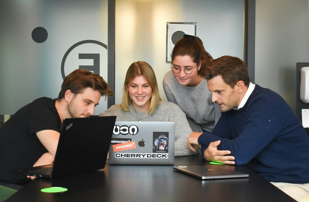 Quattro persone riunite attorno a un portatile in un ufficio, mentre guardano lo schermo